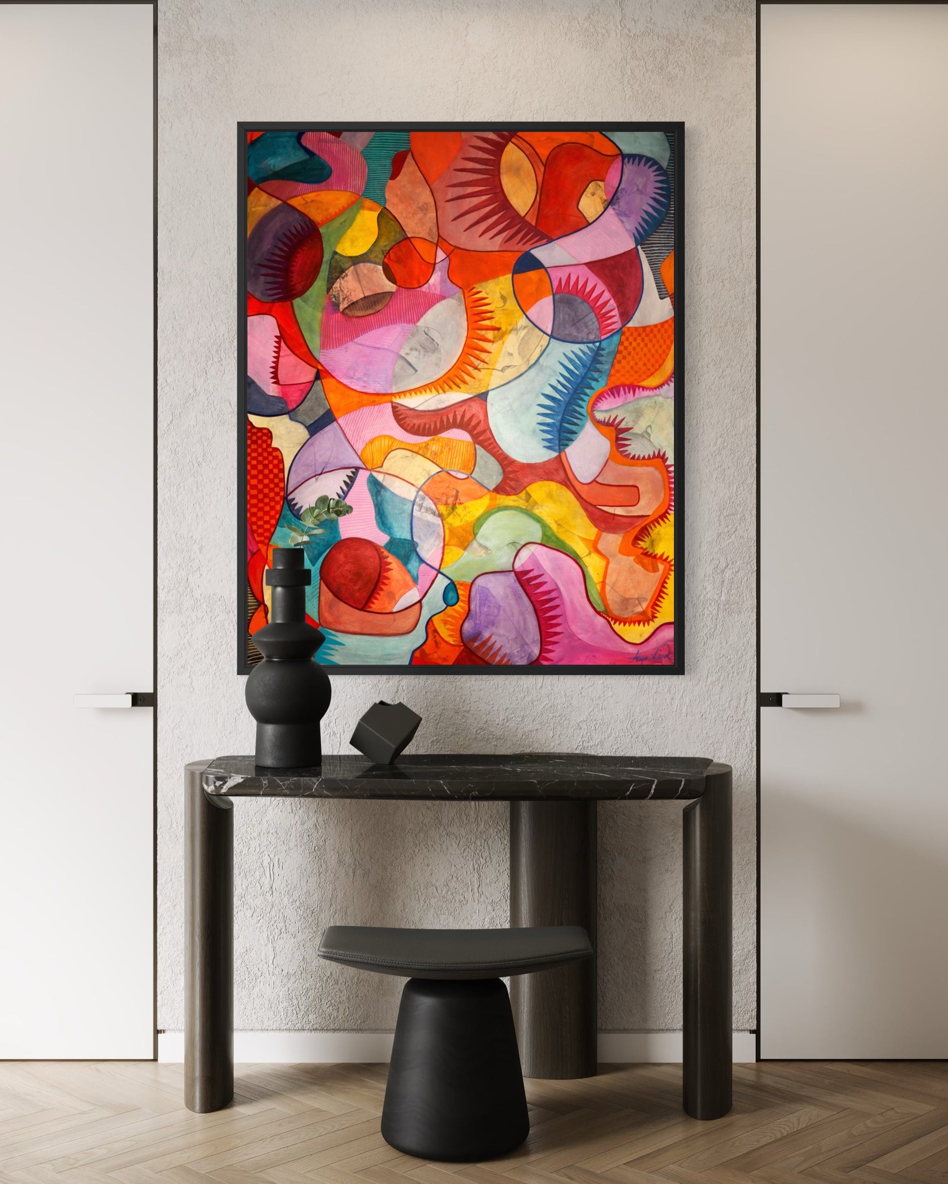 A colorful abstract canvas print with vibrant curved shapes in pink, orange, yellow, red, and blue, displayed on a textured light gray wall above a dark console table in a modern interior setting.