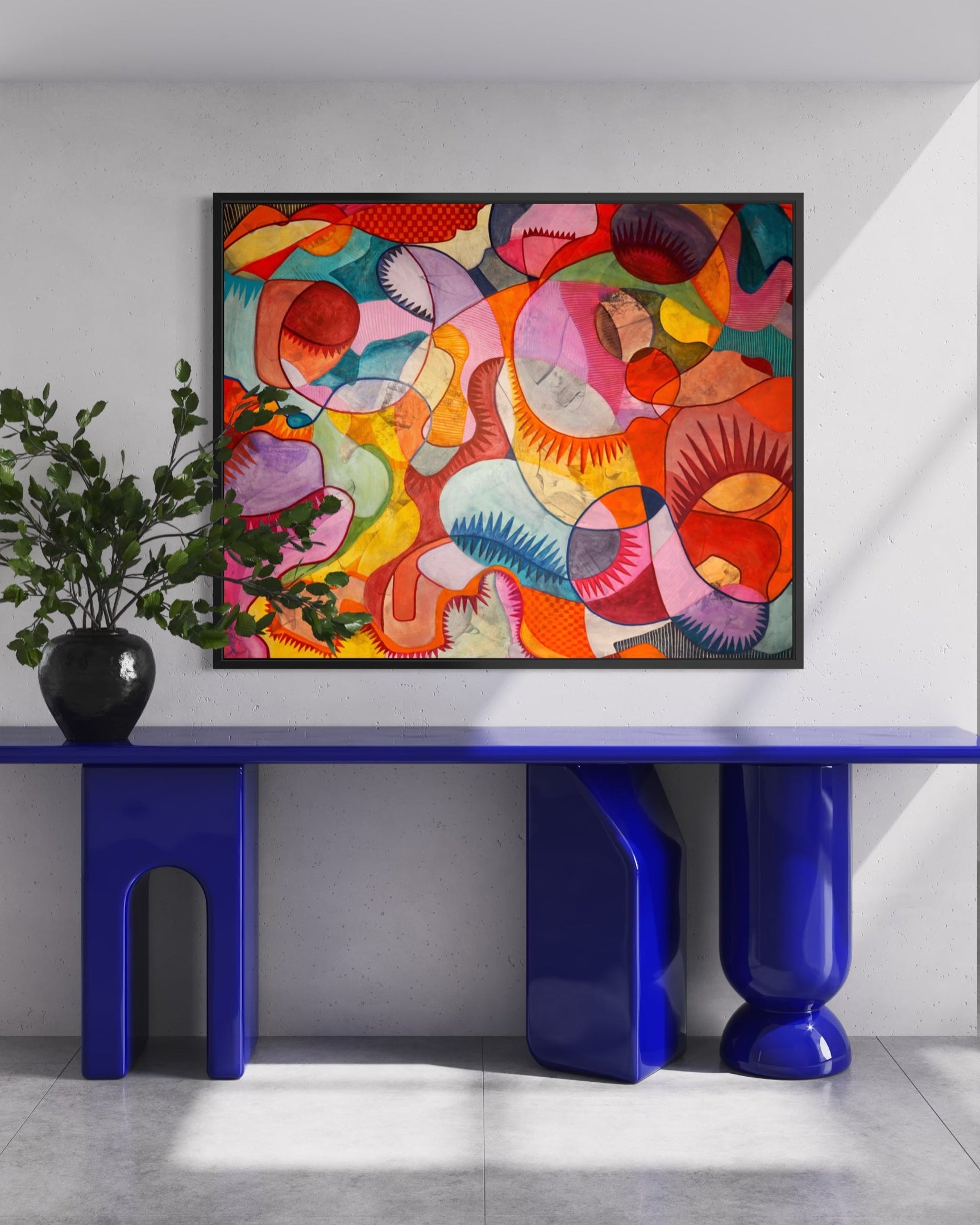 A colorful abstract canvas print with organic shapes in pink, orange, yellow, green, and blue, displayed on a white wall above a glossy blue console table with sculptural legs in a modern room.