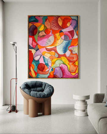 A colorful abstract canvas print with swirling organic shapes in pink, orange, yellow, blue, and red, displayed on a white wall in a modern living room setting.